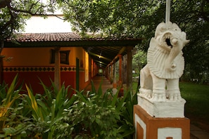 A pathway leading to a building with a tiled roof and a statue of a lion. - Indeco Mahabalipuram (Tirukalukundram)