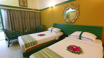 A hotel room with two beds, green headboards, a mirror, a green chair, and a small table with a plant.