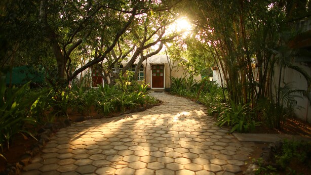 A paved pathway leading to a building with a door, surrounded by lush greenery and trees. - Indeco Mahabalipuram (Tirukalukundram)