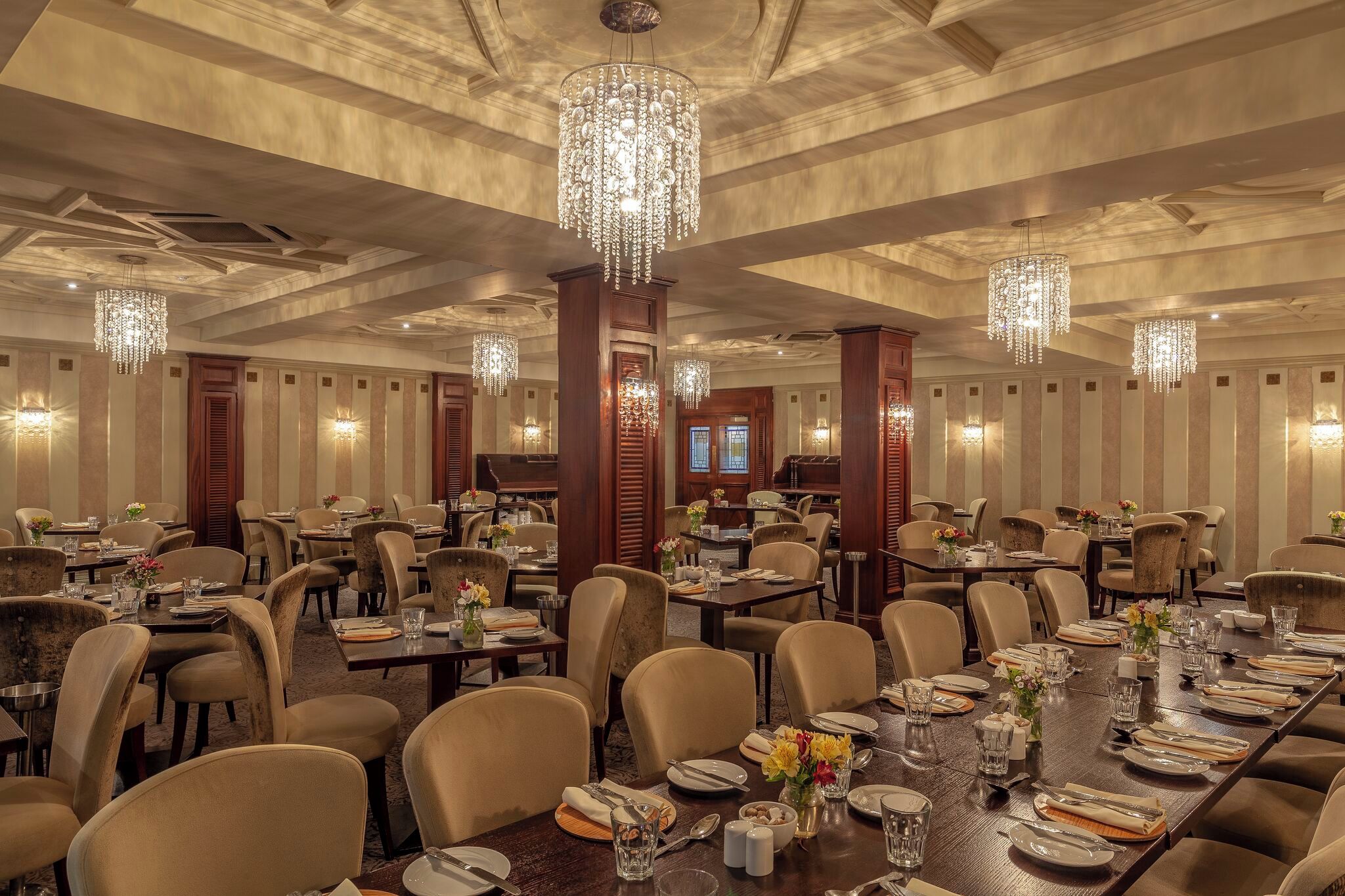 A spacious dining area with multiple tables set for meals, elegant chandeliers, and a classic interior design.