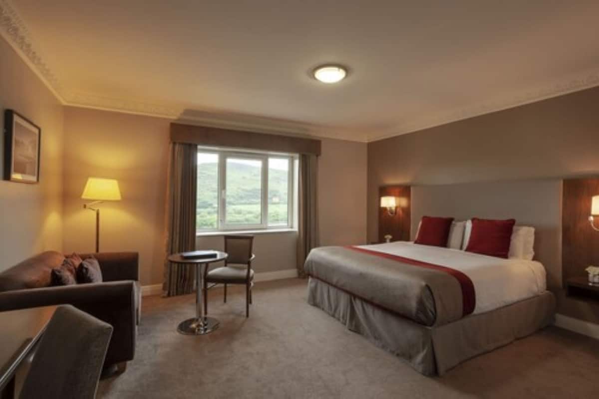 Une chambre d’hôtel avec un lit, un bureau, une chaise, une fenêtre et une lampe.