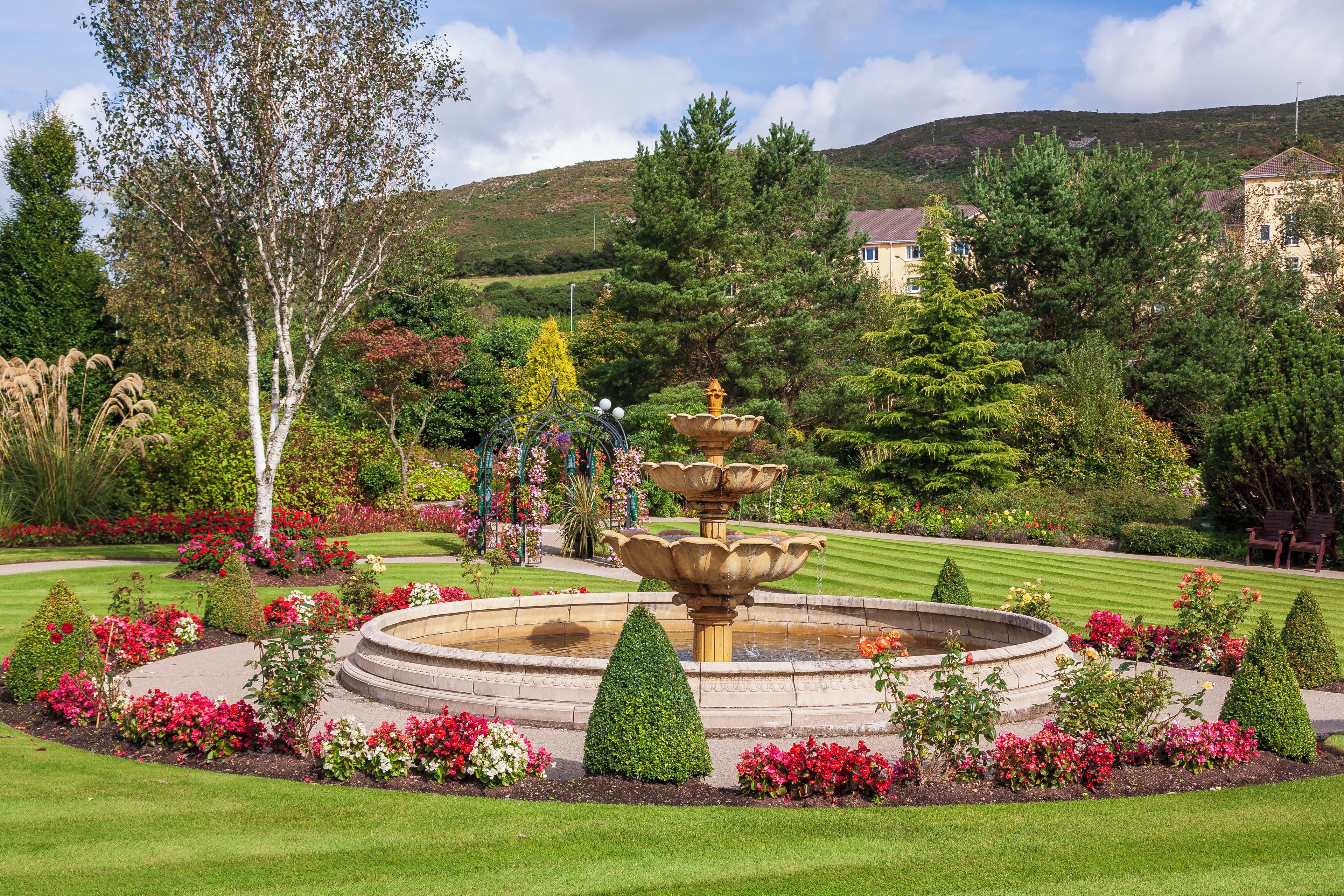 A landscaped garden with a central fountain, manicured lawns, and a variety of flowering plants.