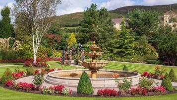A landscaped garden with a central fountain, manicured lawns, and a variety of flowering plants.