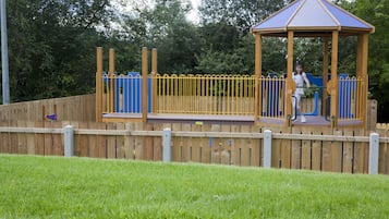 Children can play safely within the fenced playground area featuring a wooden play structure.