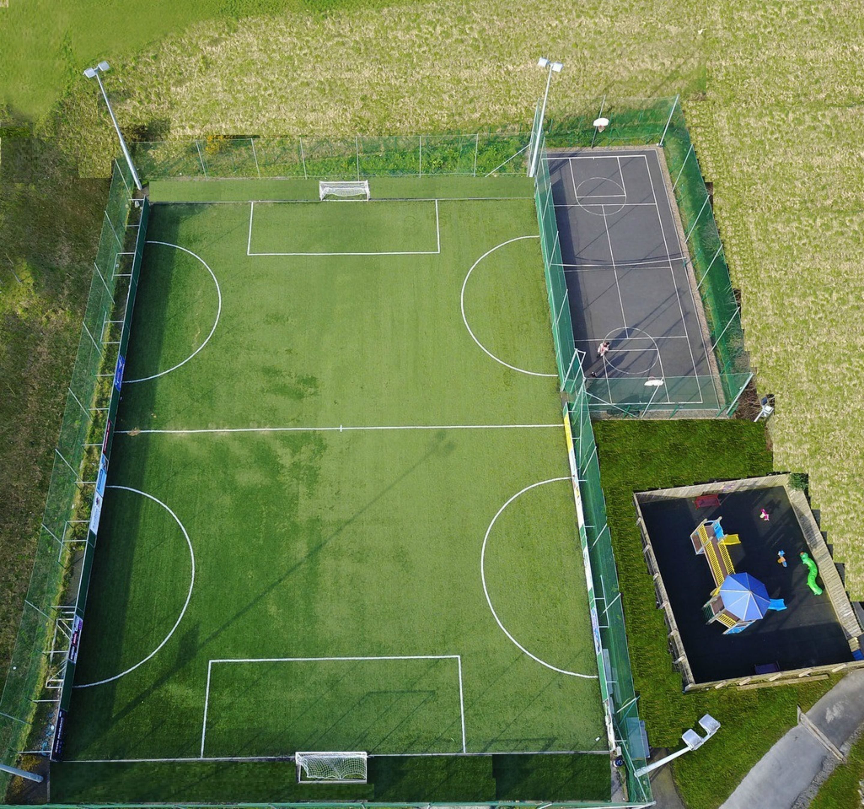 Vista aérea de um complexo esportivo com um campo de futebol, quadra de basquete e piscina.