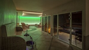 Un área de spa con una pared iluminada en verde, sillones reclinables y una puerta de vidrio que da al exterior.