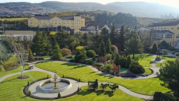 Un hotel con césped cuidado, una fuente central y un edificio grande al fondo.