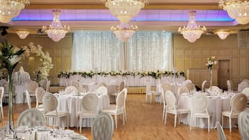 Une salle de banquet avec de nombreuses tables dressées pour le repas, décorées de nappes blanches et de chaises élégantes.