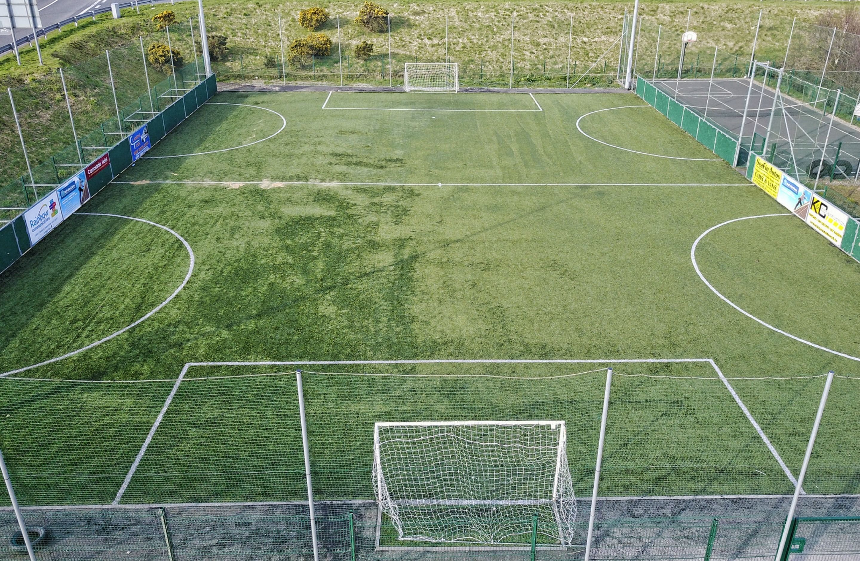 Un terrain de football avec des poteaux de but, des panneaux publicitaires et une clôture verte qui l’entoure.