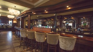 Un área de bar con taburetes de madera, una barra pulida y un espejo que refleja la barra.
