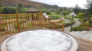 Un jacuzzi con terraza de madera y vistas a un jardín ajardinado con un pabellón.