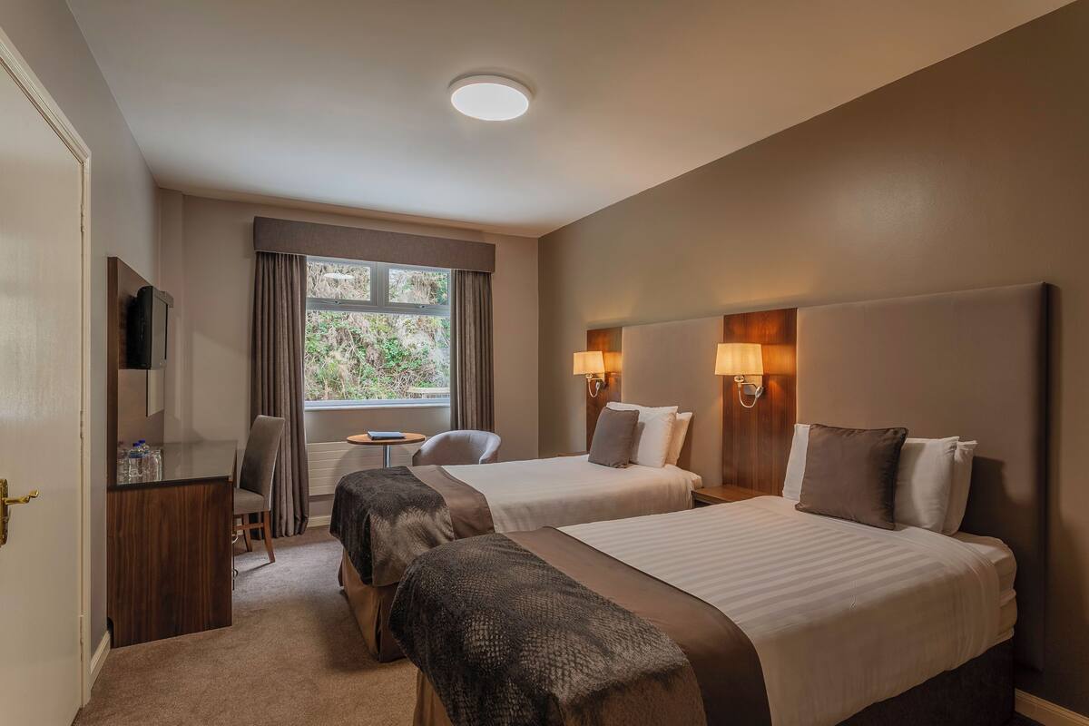 Une chambre d’hôtel avec deux lits, un bureau, une chaise, une télévision et une fenêtre avec des rideaux.