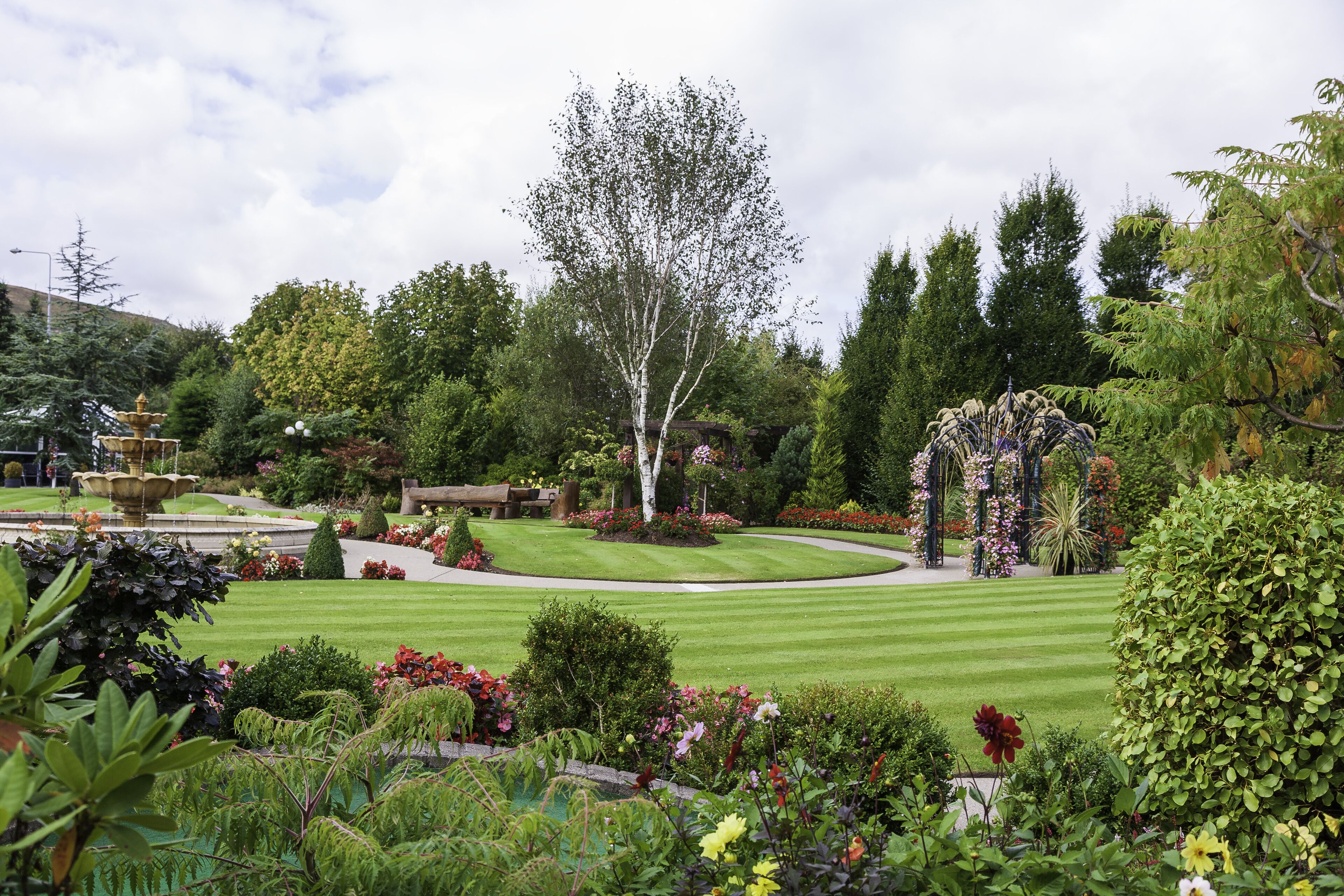 A well-maintained garden with a fountain, neatly trimmed grass, and various flowering plants.