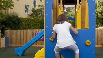A child climbing a blue climbing structure with yellow handholds.