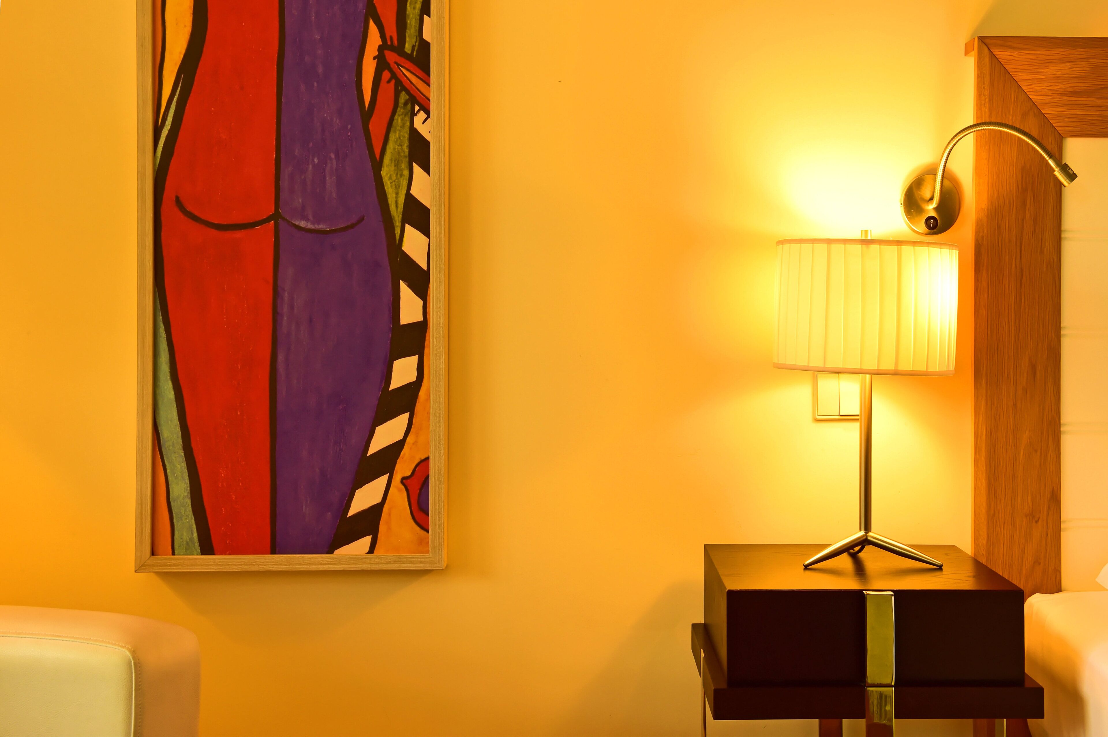 Um quarto com um quadro na parede, uma luminária sobre uma mesa e uma cadeira.