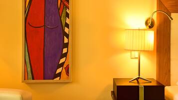 Um quarto com um quadro na parede, uma luminária sobre uma mesa e uma cadeira.