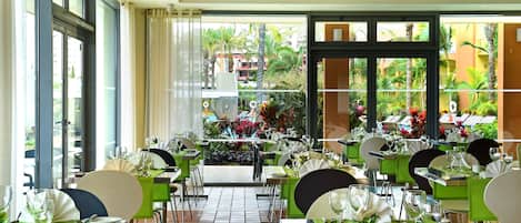 Un restaurante con varias mesas, sillas y vistas a una piscina y follaje exterior.