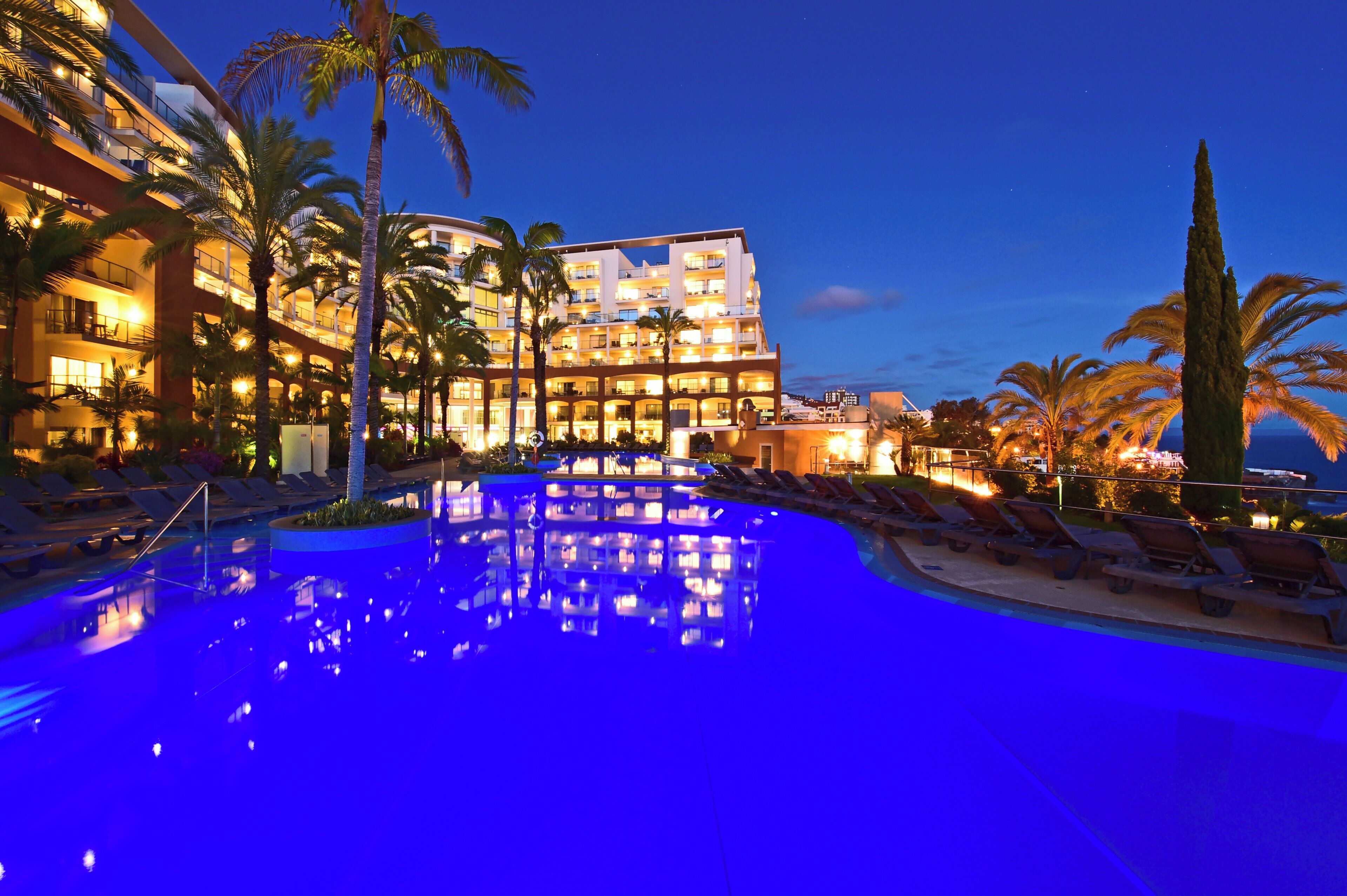 A hotel with a pool, palm trees, and a night sky.