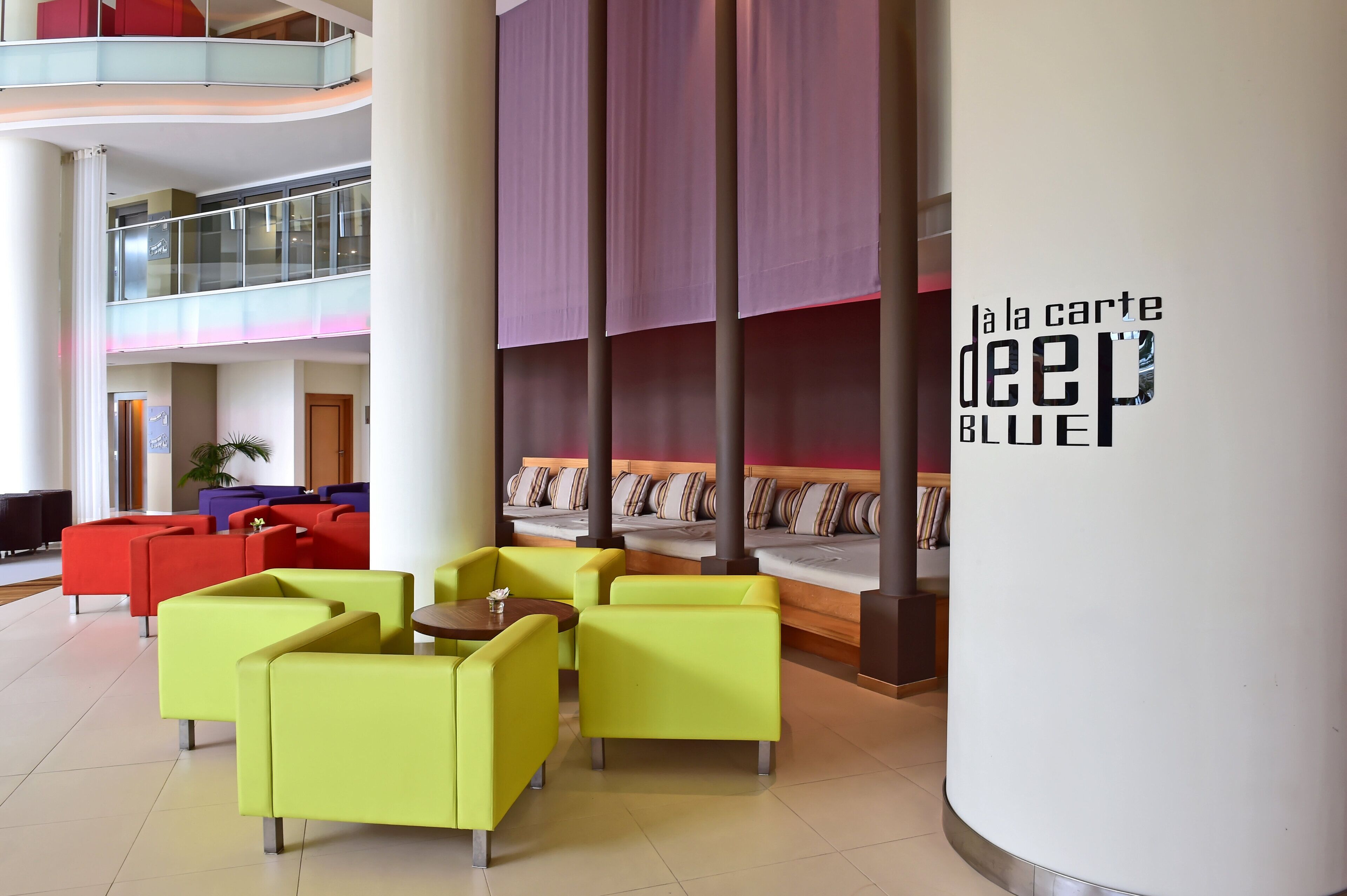 A modern lobby with a seating area featuring yellow chairs, a high ceiling, and a visible staircase.