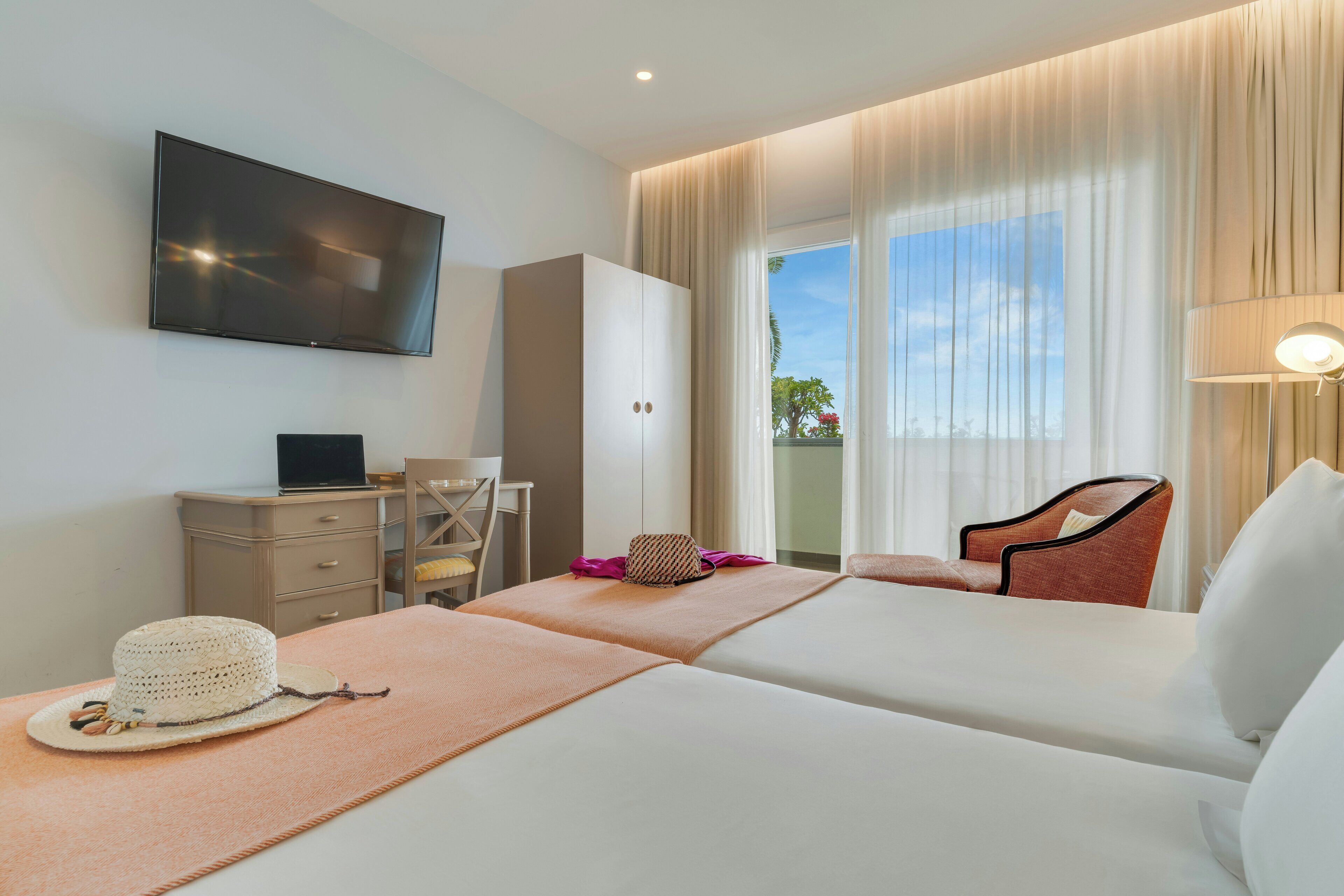 A hotel room with a bed, a desk, a TV, a chair, and a window with curtains.