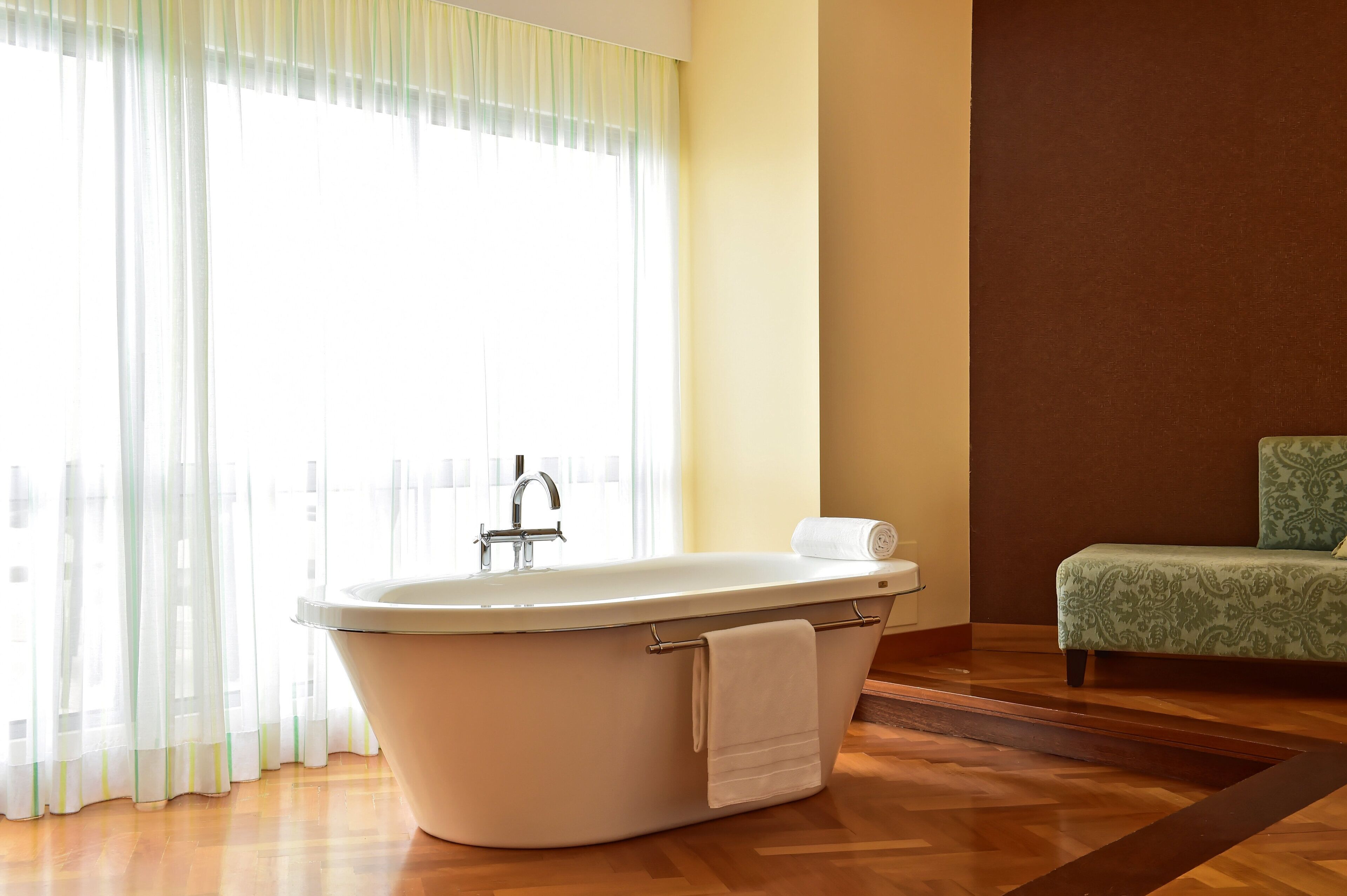 Une salle de bain avec une baignoire sur pieds, un porte-serviettes et un banc à motifs verts.