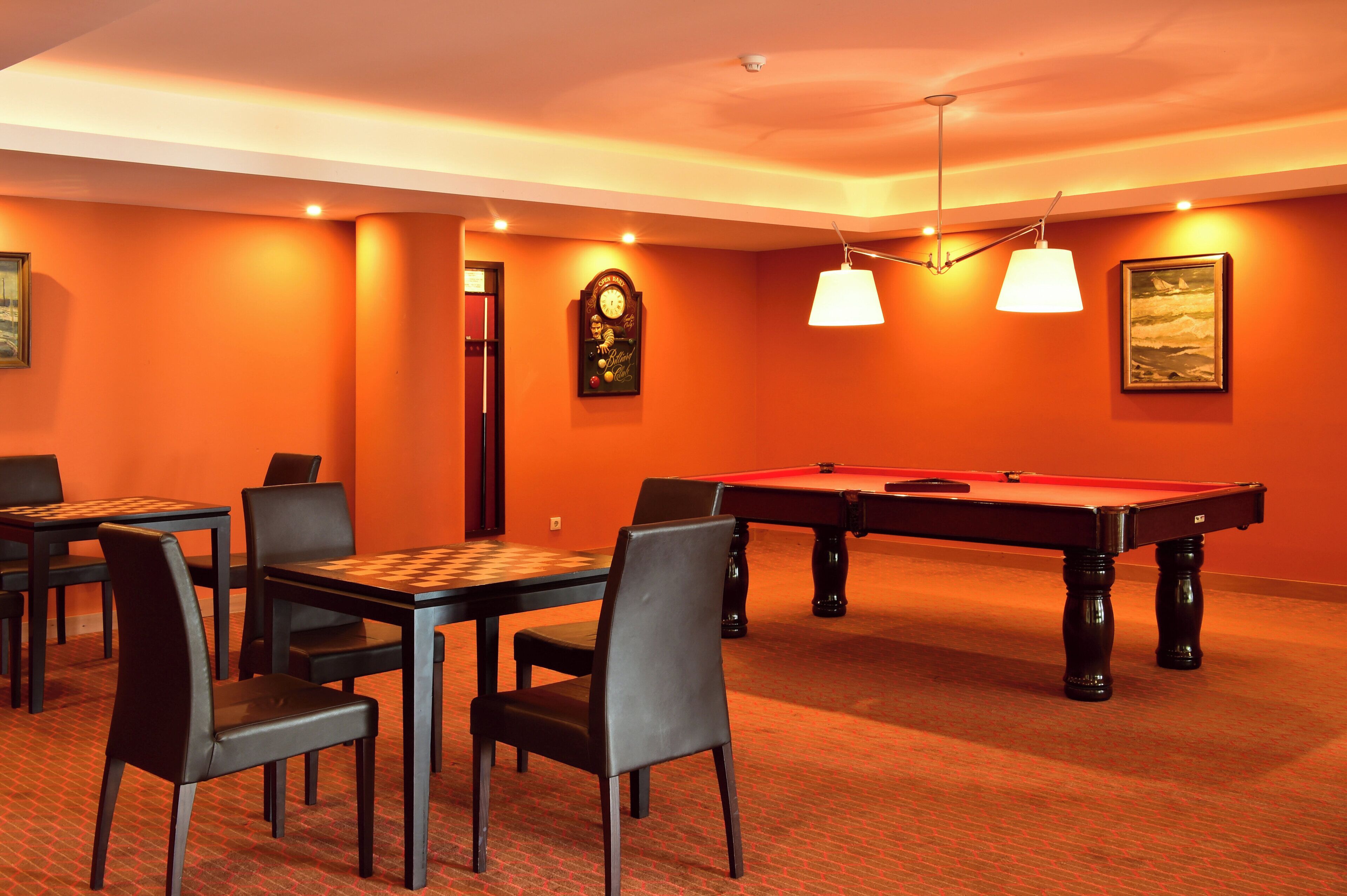 A billiards room with a pool table, chairs, and a clock on the wall.