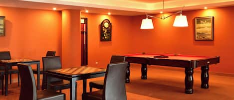 Una sala de billar con mesa de pool, sillas y un reloj en la pared.
