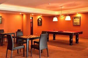 A billiards room with a pool table, chairs, and a clock on the wall.