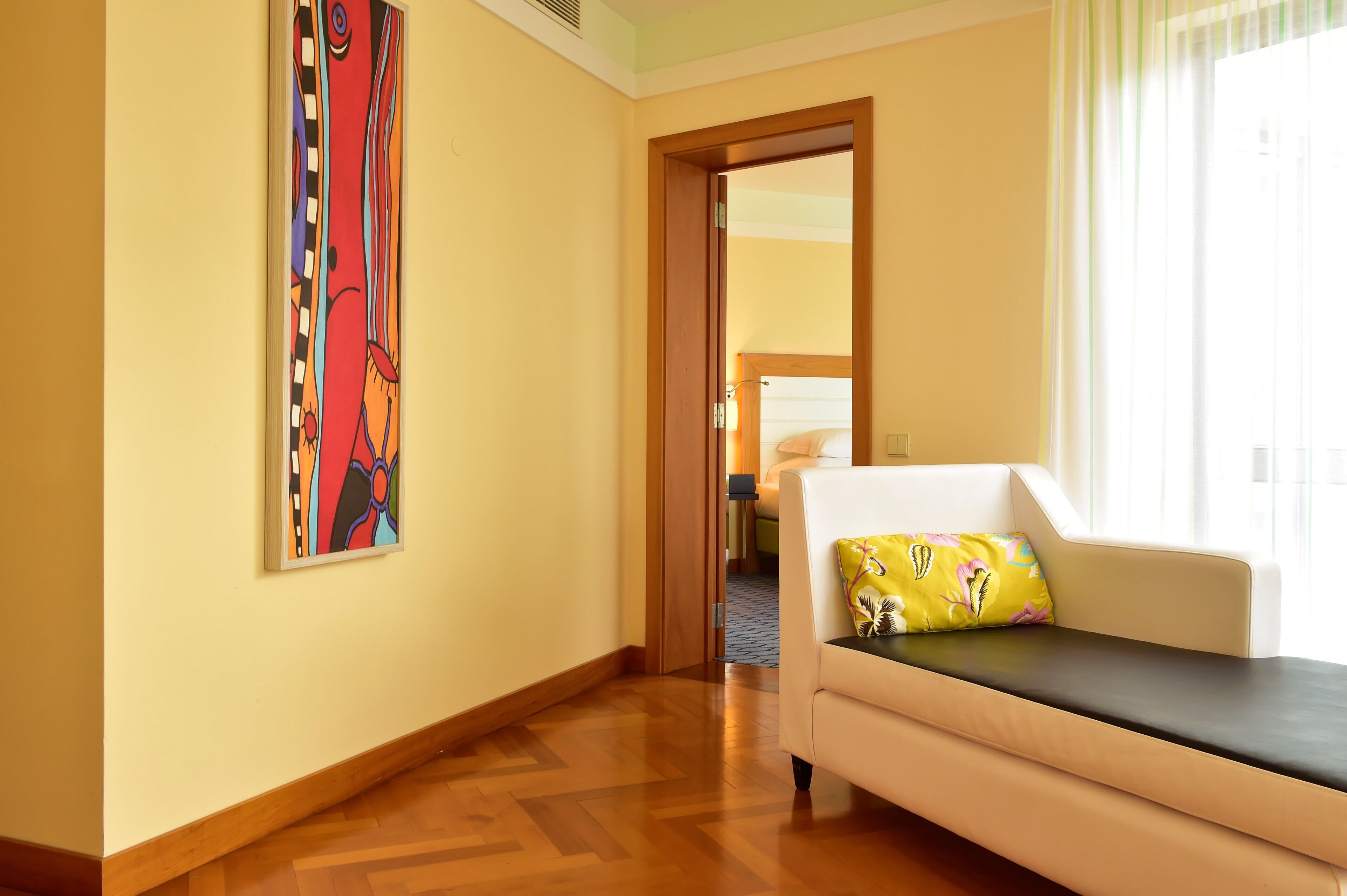 Une chambre d’hôtel avec un canapé, un tableau au mur et une vue sur l’extérieur, visible à travers une porte ouverte.