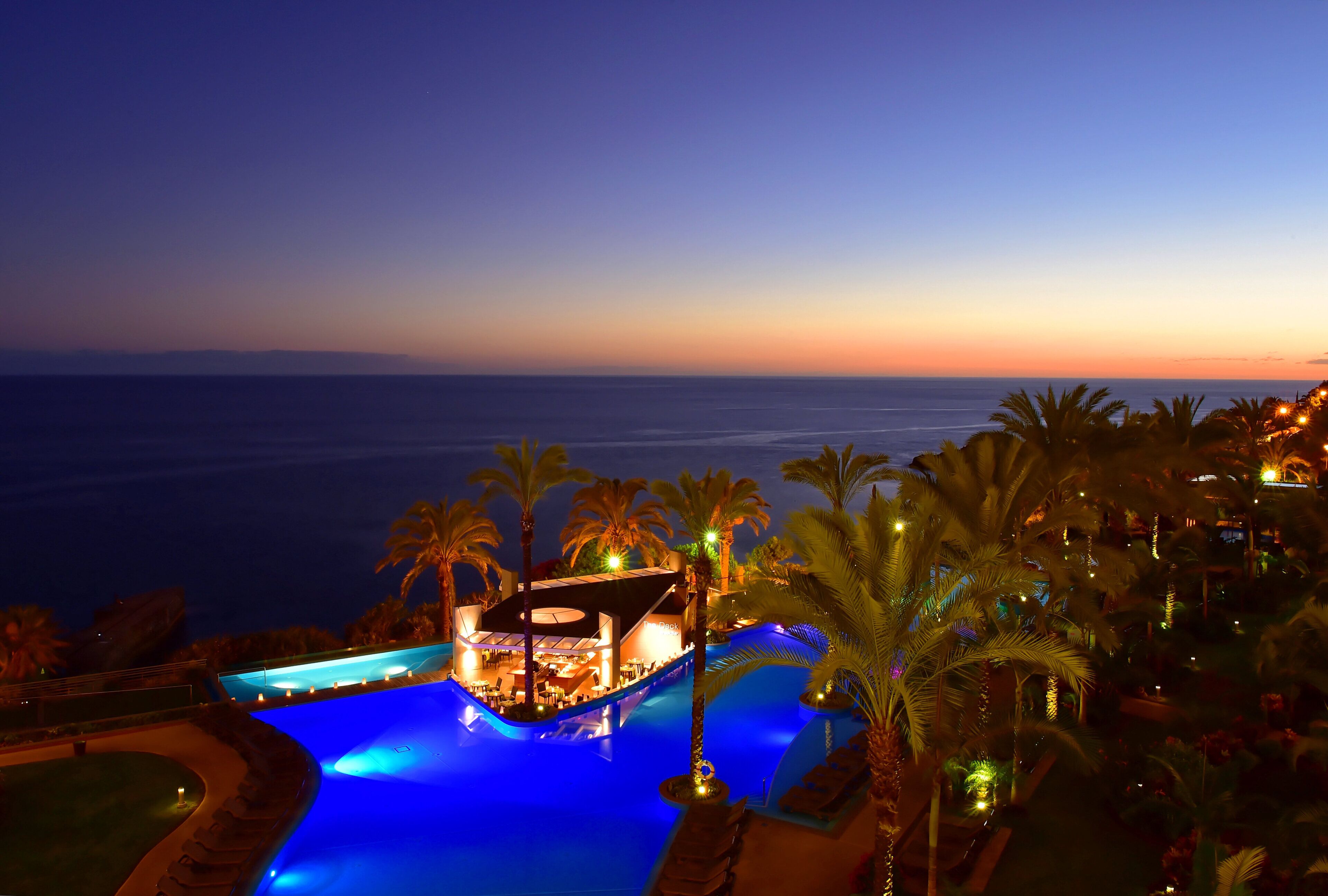 A pool area with a view of the ocean at dusk.
