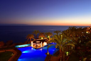 Un área de piscina con vista al océano al anochecer.
