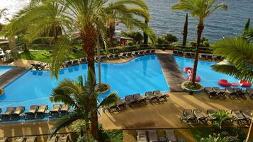 A pool with lounge chairs and palm trees, surrounded by a landscaped area with a view of the sea.