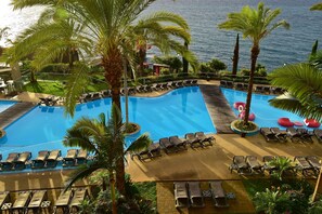Une piscine bordée de chaises longues et entourée de palmiers, le tout aménagé dans un espace paysager offrant une vue sur la mer.