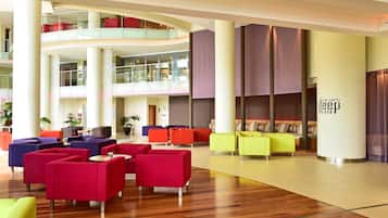 Una hall moderna con diverse zone salotto, un parapetto in vetro e un soffitto alto.