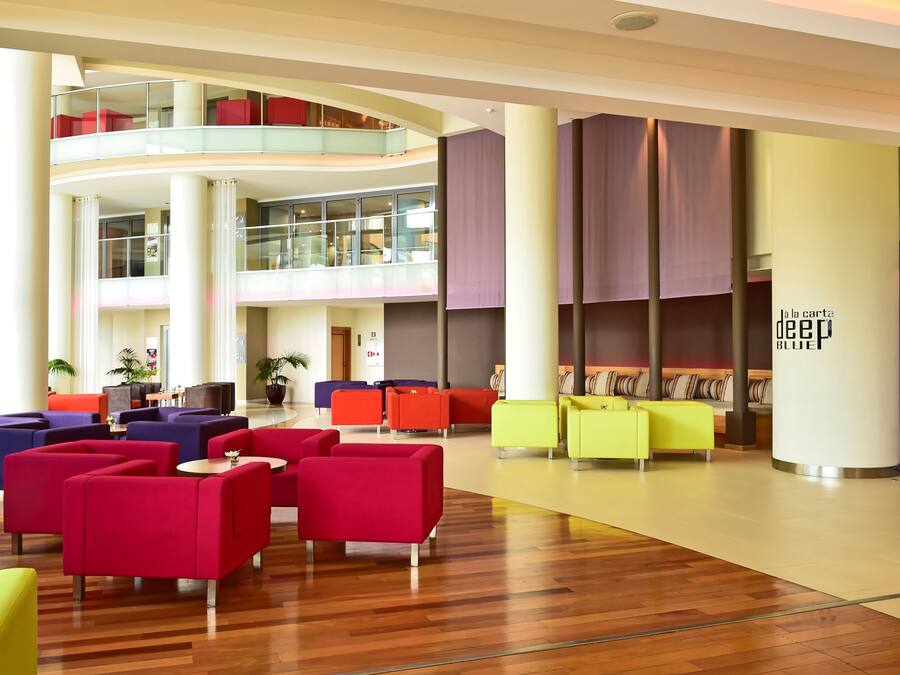A modern lobby with multiple seating areas, a glass railing, and a high ceiling.