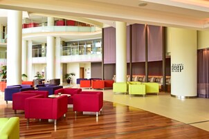 Um lobby moderno com várias áreas de estar, guarda-corpo de vidro e pé direito alto.
