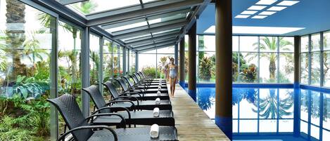 Un área de piscina techada con sillones de descanso y techo de vidrio.