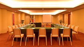A conference room with a long table, chairs, flags, and a projector screen.
