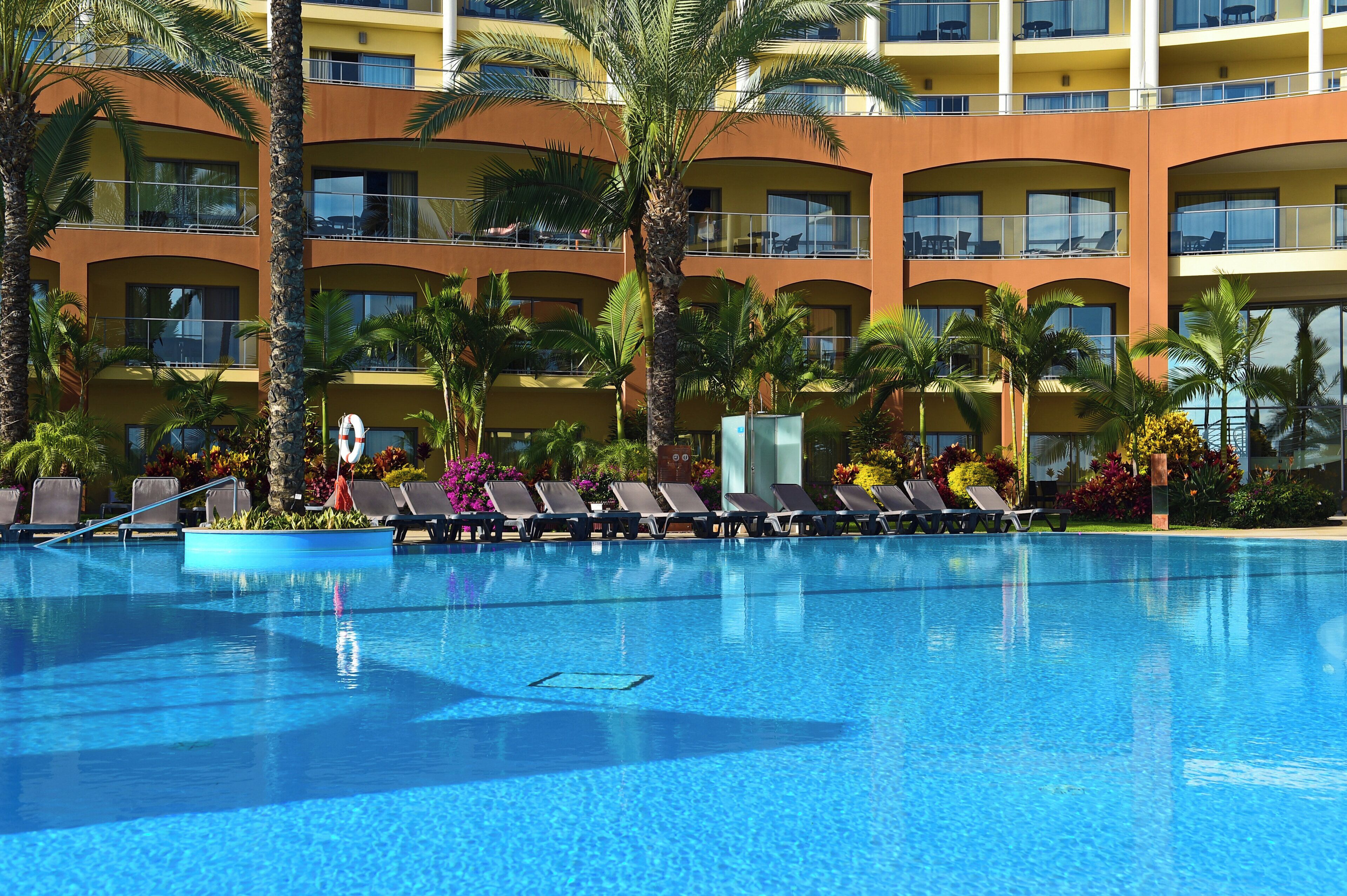 Une piscine d’hôtel avec plusieurs niveaux de balcons, entourée de palmiers et de chaises longues.