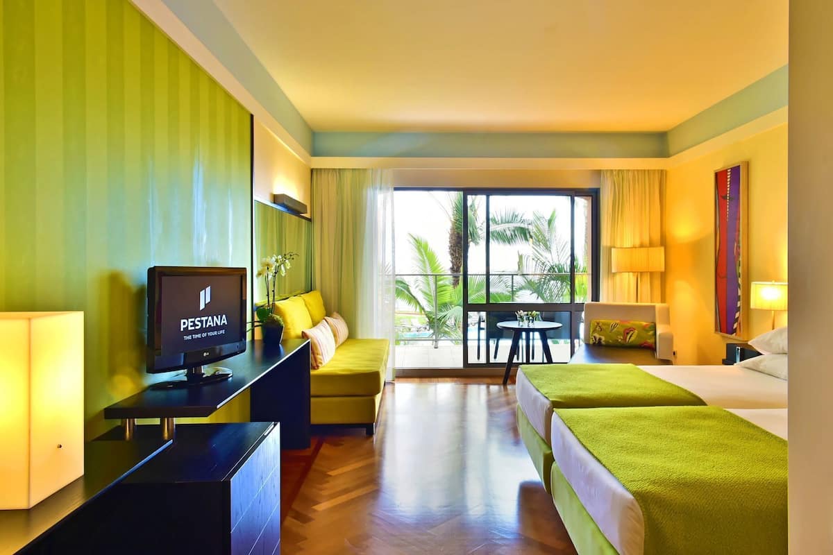 A hotel room with a bed, a desk with a computer, a sofa, and a view of palm trees.
