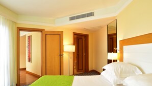 A hotel room with a bed, a bedside lamp, a door, and a window with curtains. - Pestana Promenade Ocean Resort Hotel (Funchal)
