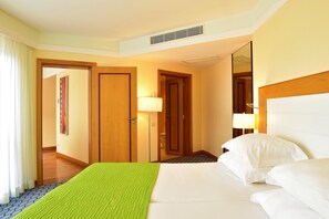 A hotel room with a bed, a bedside lamp, a door, and a window with curtains. - Pestana Promenade Ocean Resort Hotel (Funchal)