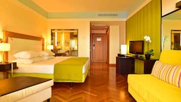 Una camera d'albergo con un letto, un divano, una scrivania con televisore e un bagno con specchio e lavandino.