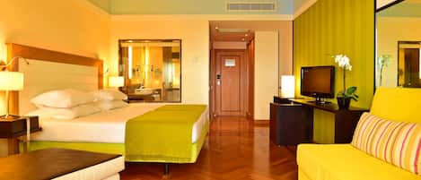 A hotel room with a bed, a sofa, a desk with a TV, and a bathroom with a mirror and sink.