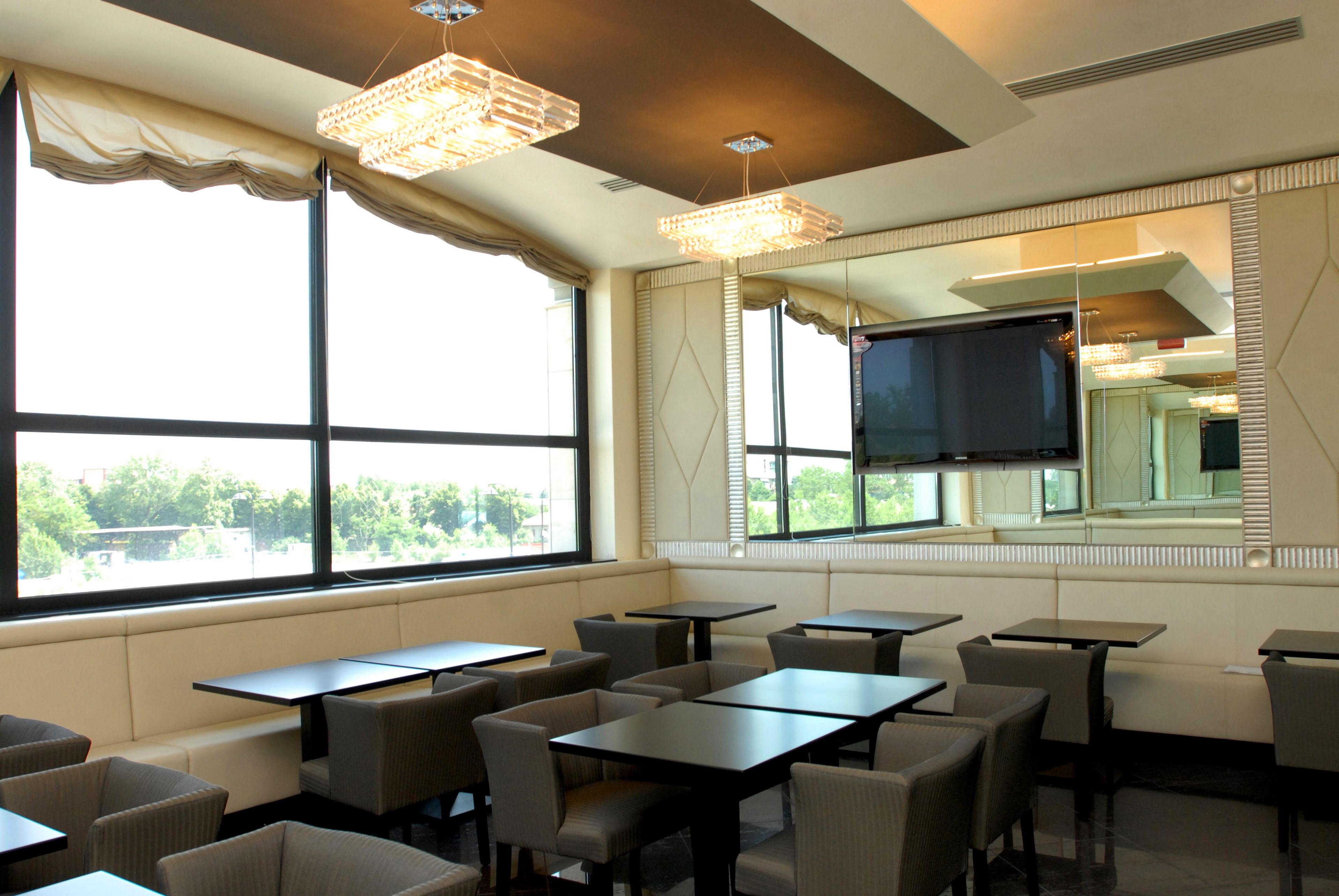 A dining area with tables and chairs, large windows with curtains, and a large mirror on the wall.