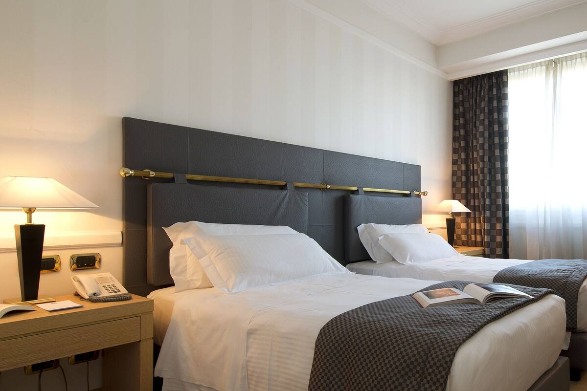 Habitación de hotel con dos camas, un escritorio con lámpara, una silla, una mesita con frutero y un espejo.