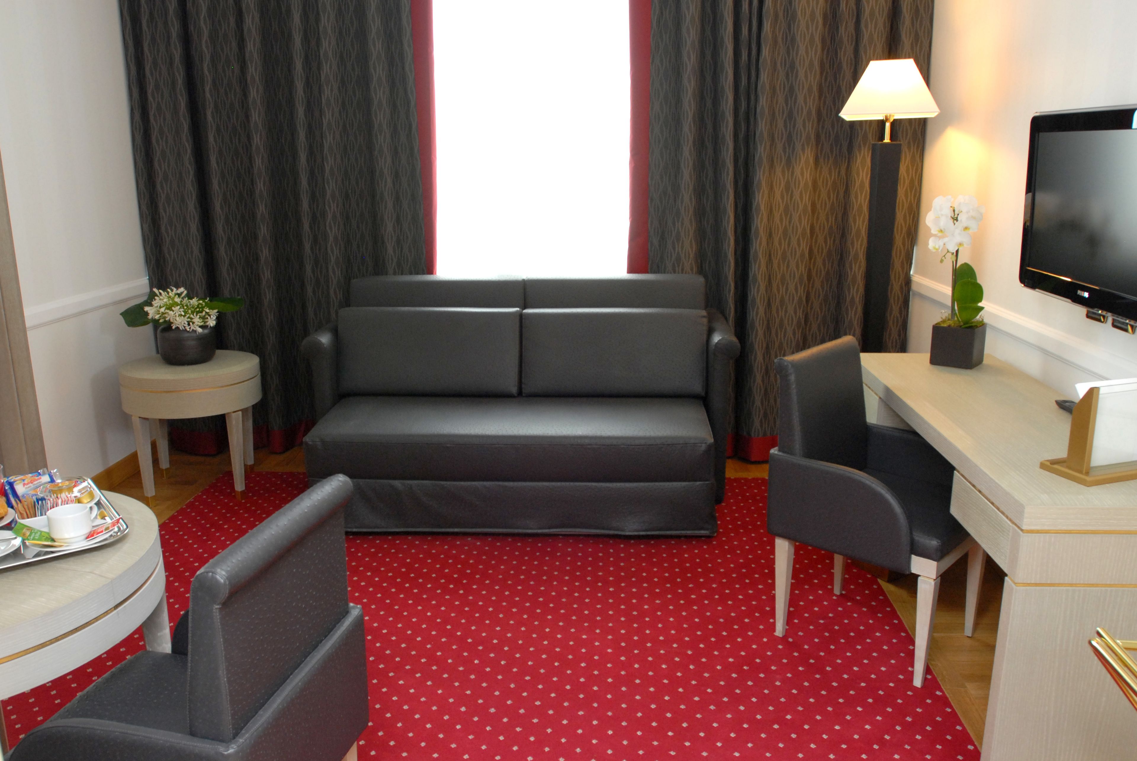 A hotel room with a grey sofa, a desk with a TV, a small table with a tray of breakfast items, and a red polka dot carpet.