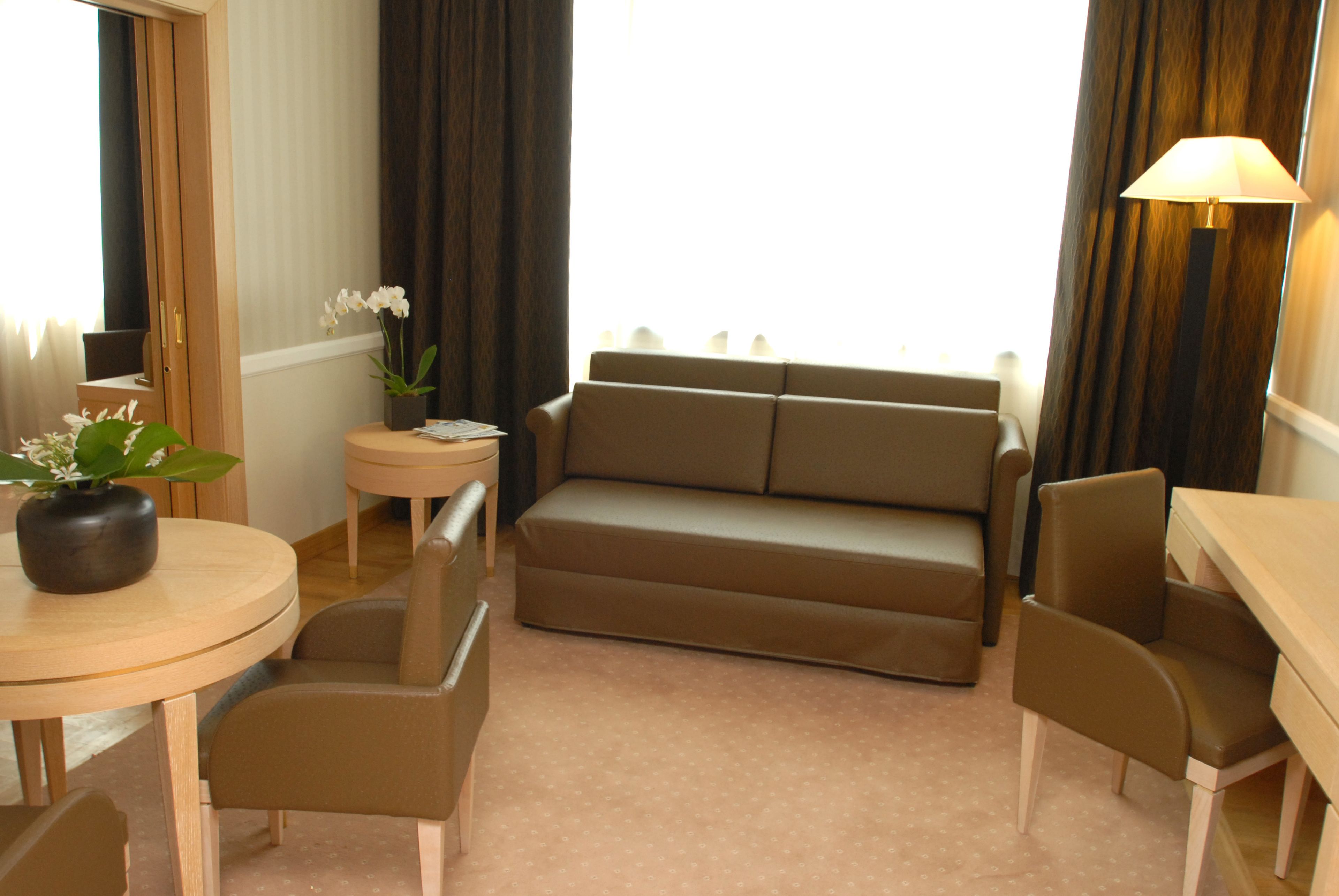 Una sala moderna con un sofá color beige, dos sillones a juego, una mesita redonda con un florero y una lámpara.