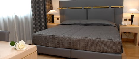 Une chambre à coucher bien rangée, avec un lit, des tables de chevet et un bureau agrémenté d’une fleur.