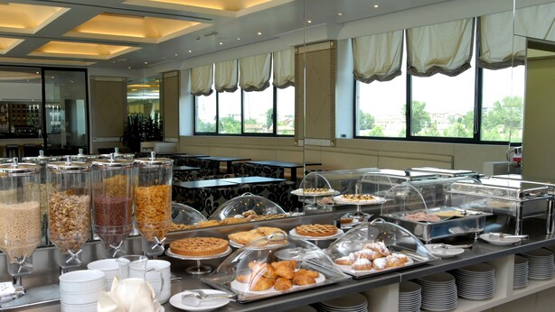 A buffet area with various food items, including pastries and cereals, arranged on a counter with a view of the outdoors through large windows. - Grand Hotel Duca di Mantova (Sesto San Giovanni)